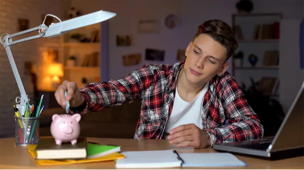 Boy student adding money to a piggy bank