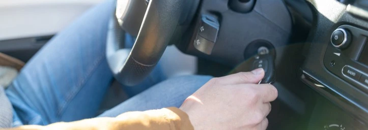 A person putting keys in a car ignition to start it