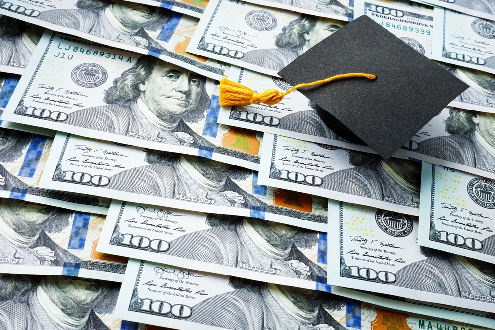 A graduation cap sitting on top of several hundred dollar bills